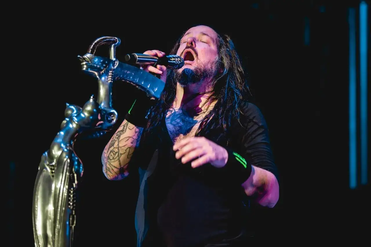 Le chanteur de Korn, Jonathan Davis, chante avec passion dans un micro, son visage illuminé par les projecteurs.