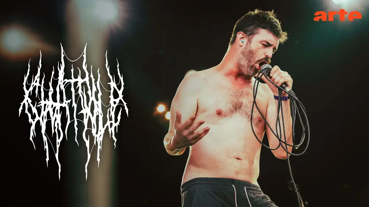 Un chanteur torse nu, micro en main, sur scène. Le logo du groupe 
