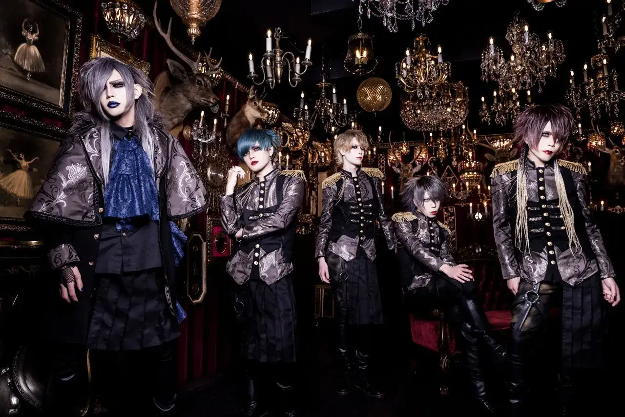 Cinq membres de X Japan posent dans un décor somptueux, ornés de tenues baroques et de maquillage extravagant.