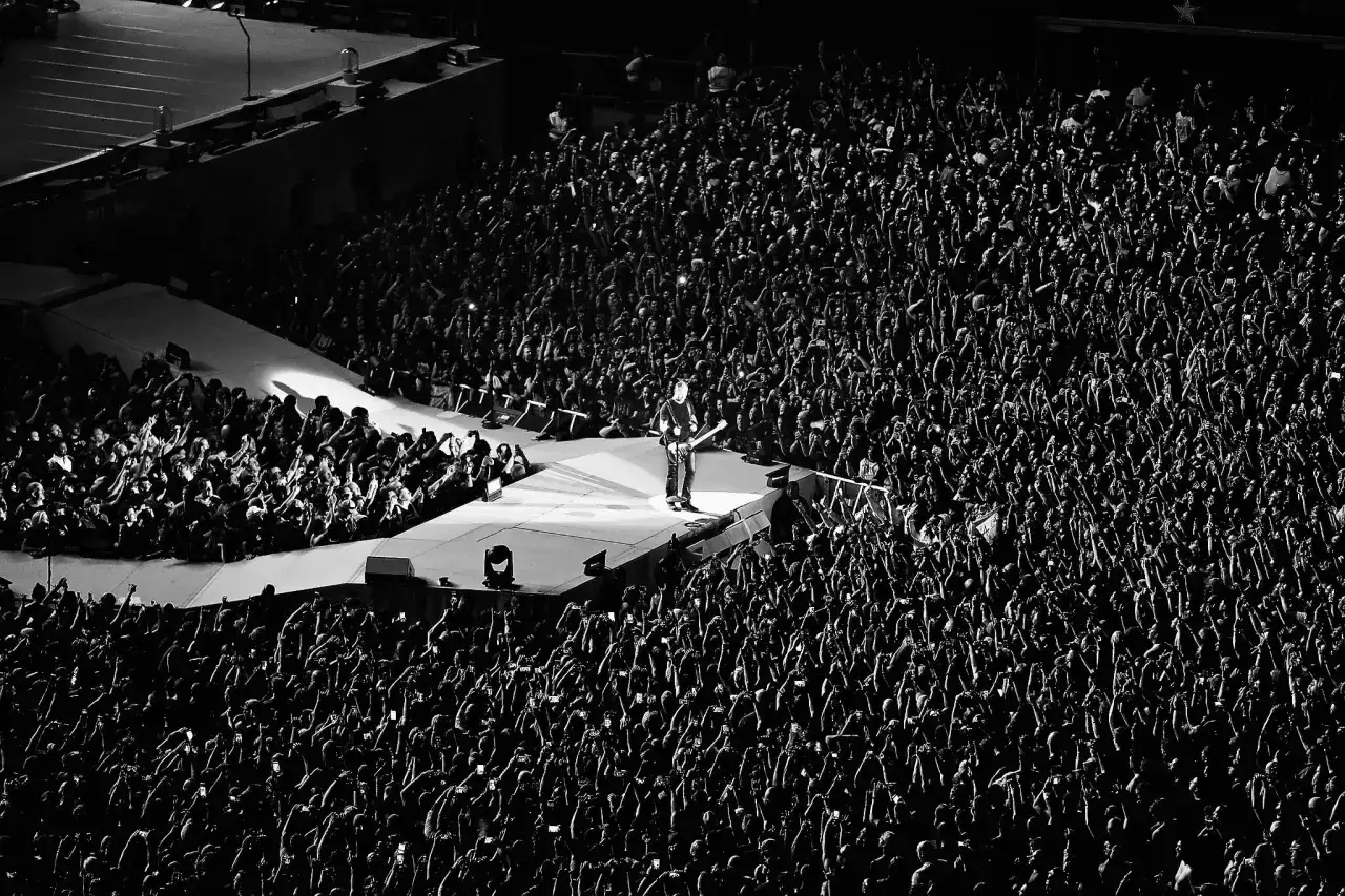 Un guitariste seul sur scène, entouré d'une foule immense aux mains levées. L'énergie d'un concert du premier groupe de metal.