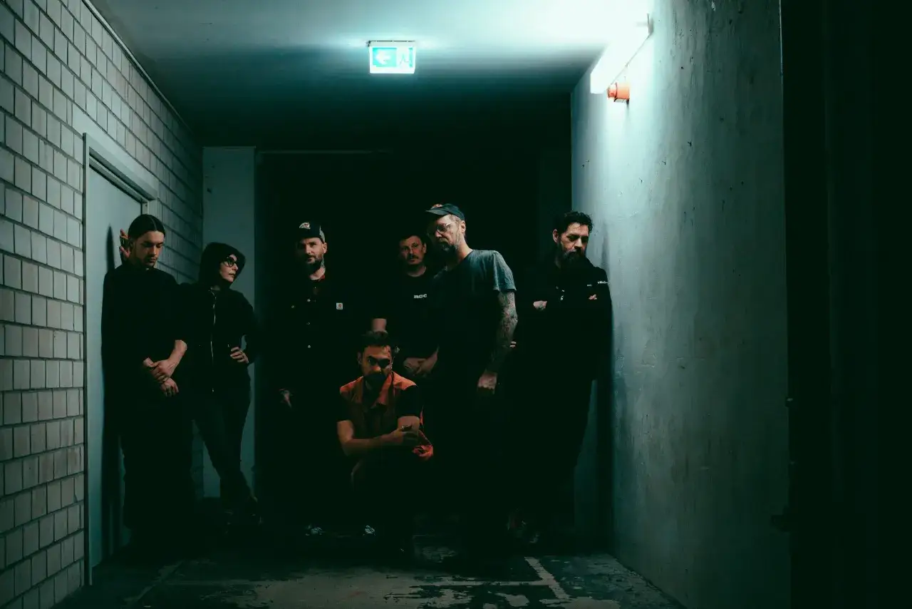 Groupe d'amis dans un couloir sombre, éclairé par une sortie de secours. Ils ressemblent à un phénix noir estropié, attendant leur renaissance.