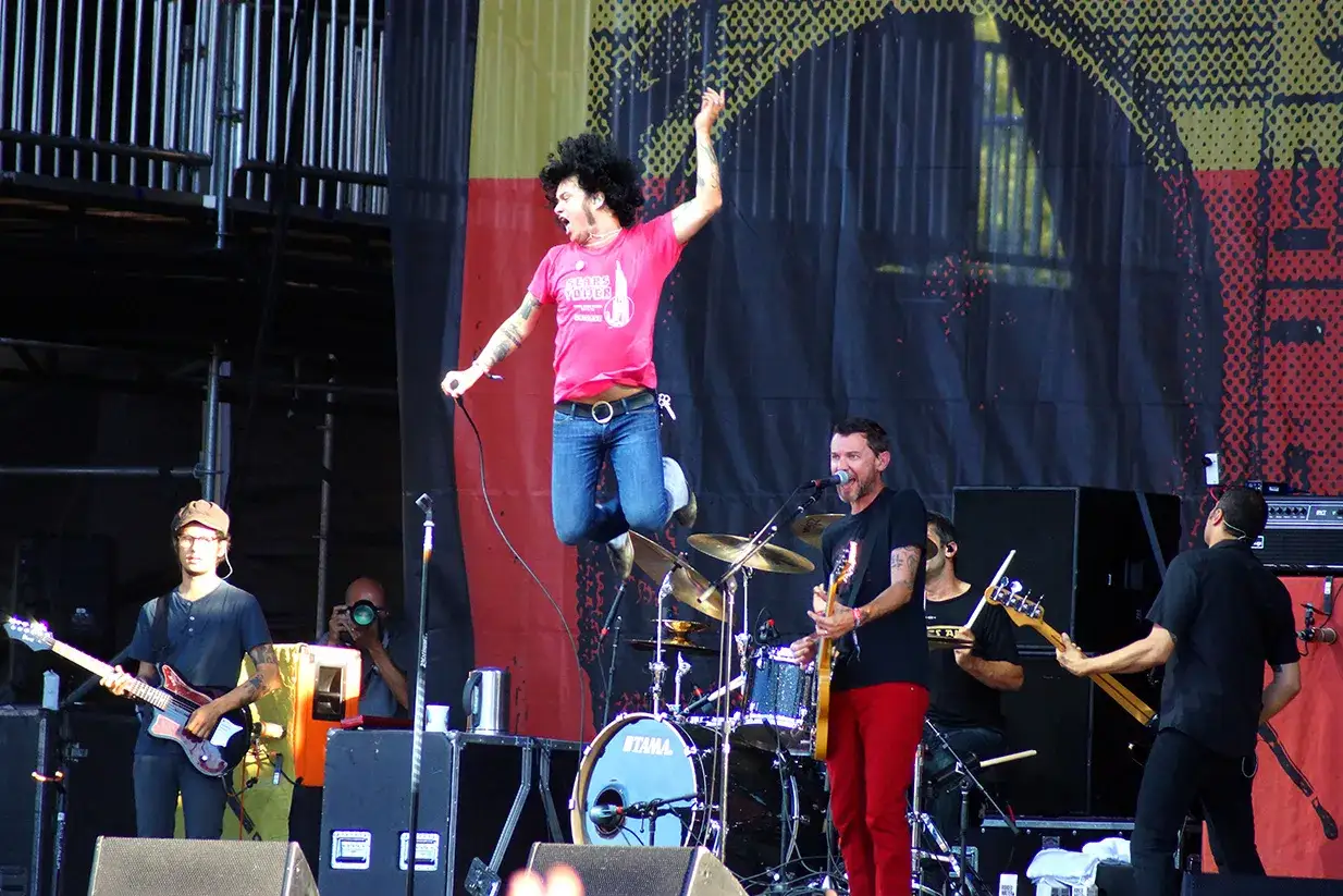 Un chanteur saute sur sc&egrave;ne, micro en main, lors d'un concert. Le groupe joue &agrave; la drive-in.