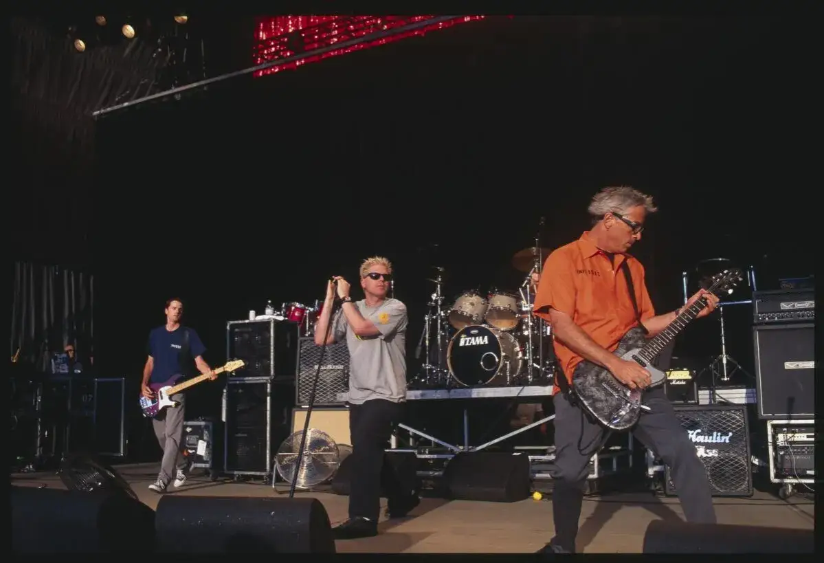 Les membres de The Offspring sur scène, Dexter Holland au micro, Noodles à la guitare, et Ron Welty à la batterie.