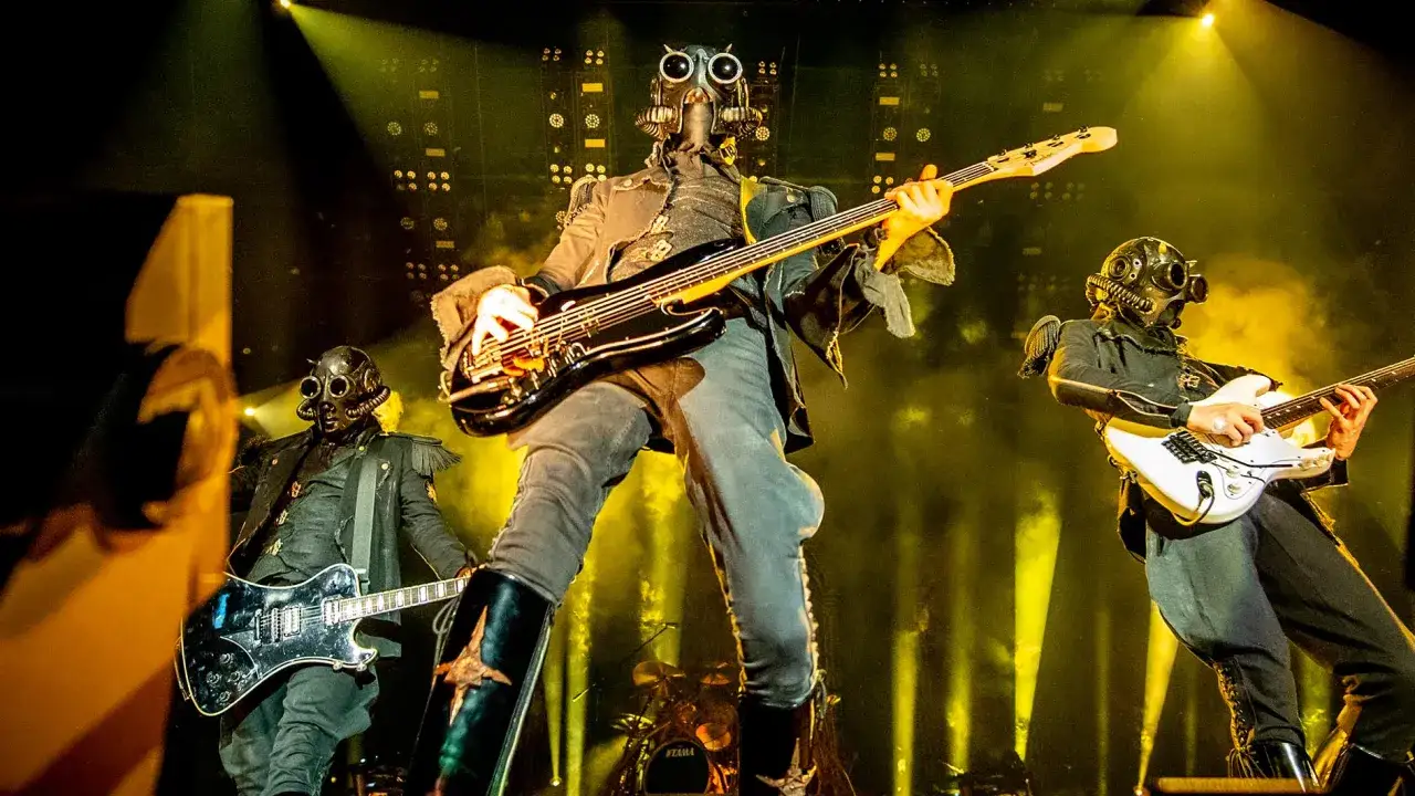Les membres du groupe Ghost jouent sur sc&egrave;ne, masqu&eacute;s et costum&eacute;s, sous des projecteurs jaunes.