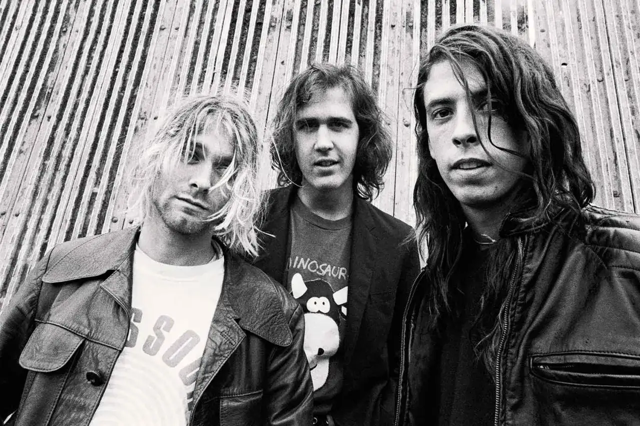 Les membres de Nirvana, Kurt Cobain, Krist Novoselic et Dave Grohl, posent devant un mur en bois.