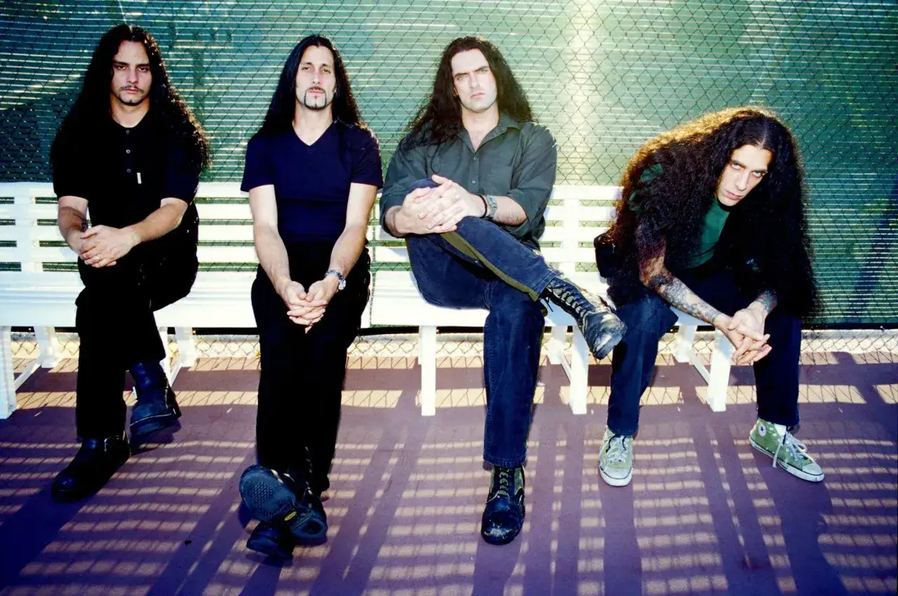 Les membres de Type O Negative posent sur un banc, leurs longs cheveux encadrant leurs visages pensifs.