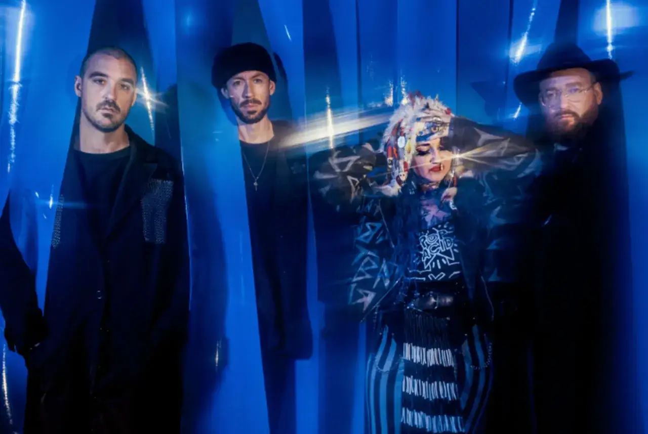 Le groupe Hiatus Kaiyote pose devant un fond bleu abstrait, avec des lumières vives créant un effet de mouvement.