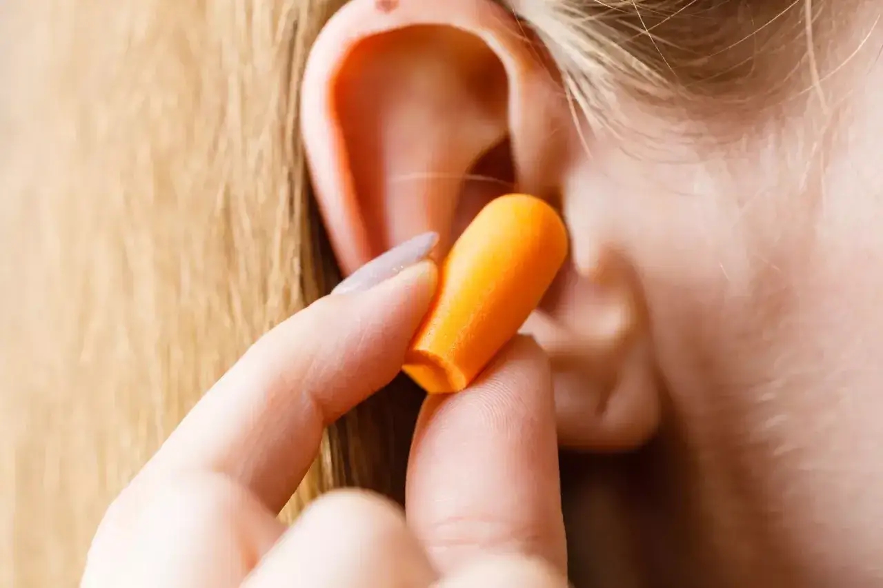 Main d'une personne insérant un bouchon d'oreille orange pour soulager l'hyperacousie.