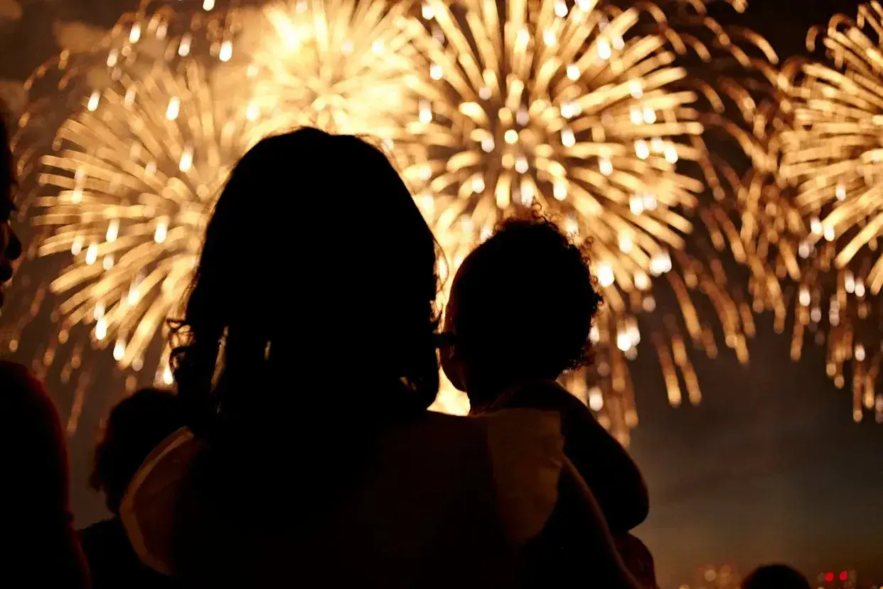 Une mère tient son enfant, admirant un feu d'artifice éclatant. Le décibel feu d'artifice résonne dans la nuit.