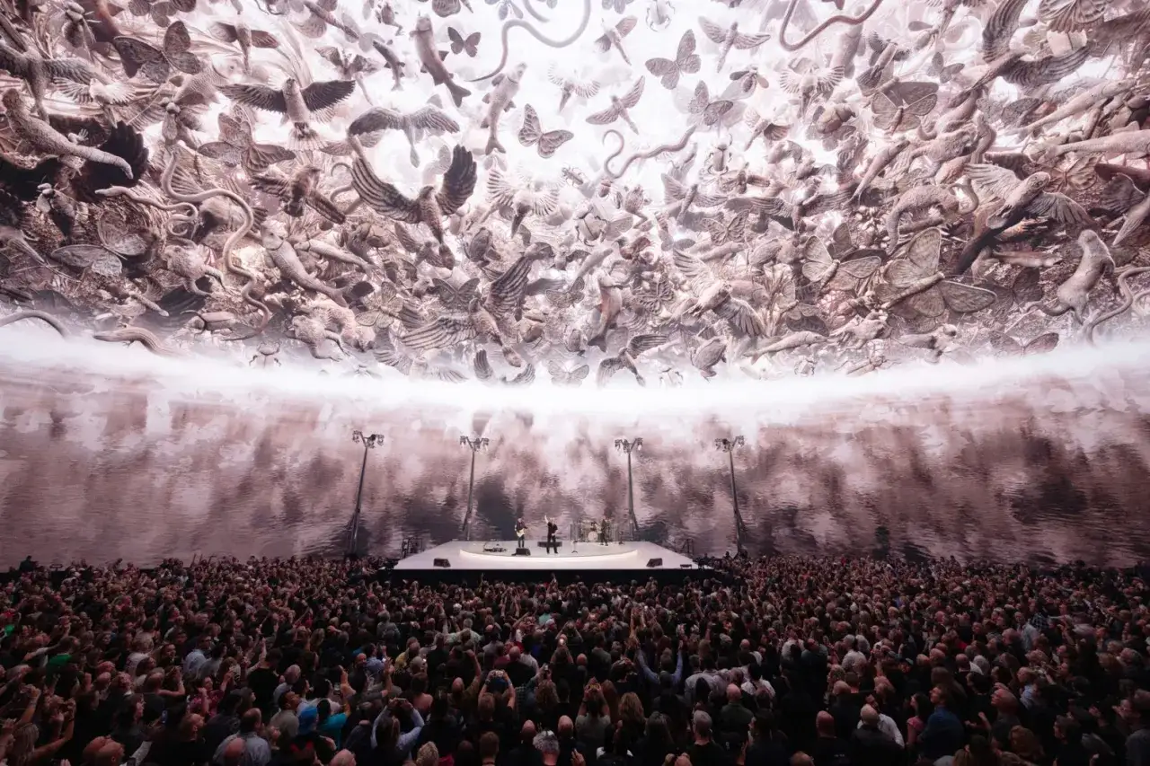Le groupe U2 en concert, sous un ciel peupl&eacute; d'une myriade d'animaux et d'insectes sculpt&eacute;s, devant une foule immense.