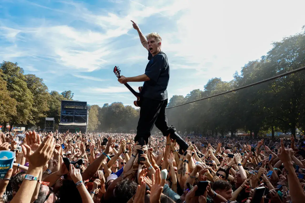 Le chanteur du groupe Last Train, porté par la foule, joue de la guitare sous un ciel bleu.