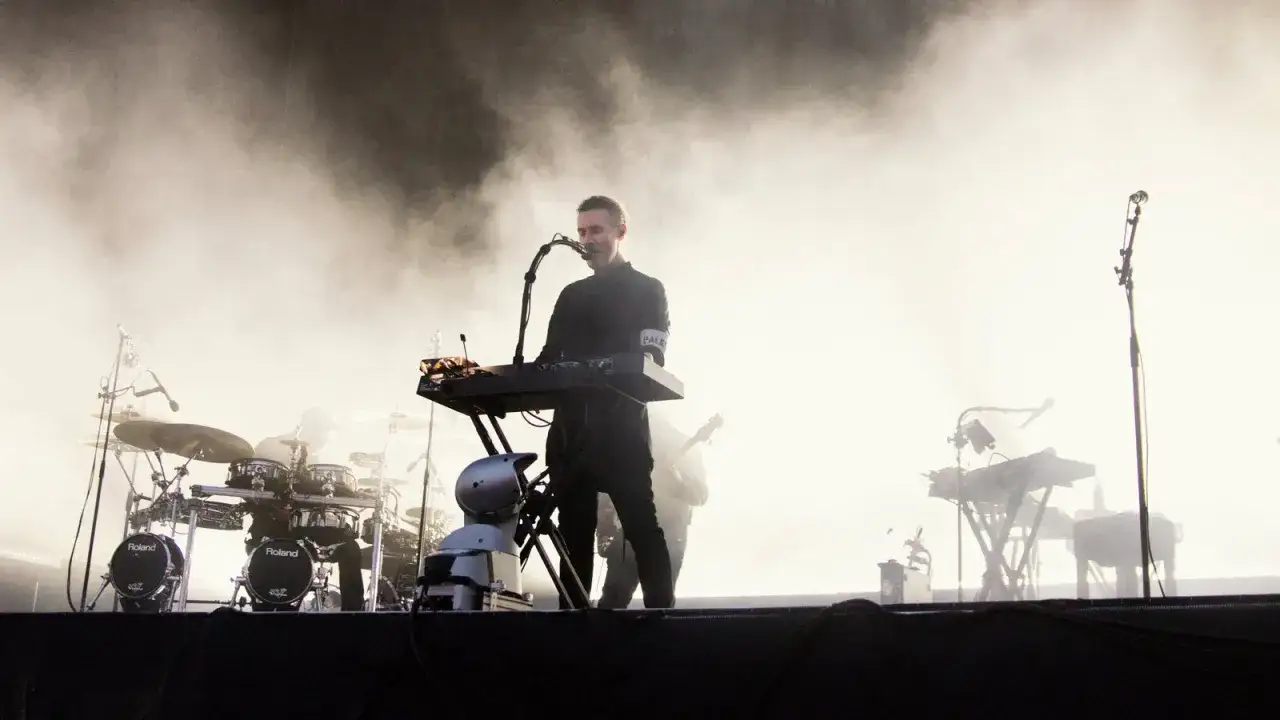 Un membre de Massive Attack joue du clavier sur sc&egrave;ne, entour&eacute; de fum&eacute;e. Un batteur est visible &agrave; gauche.