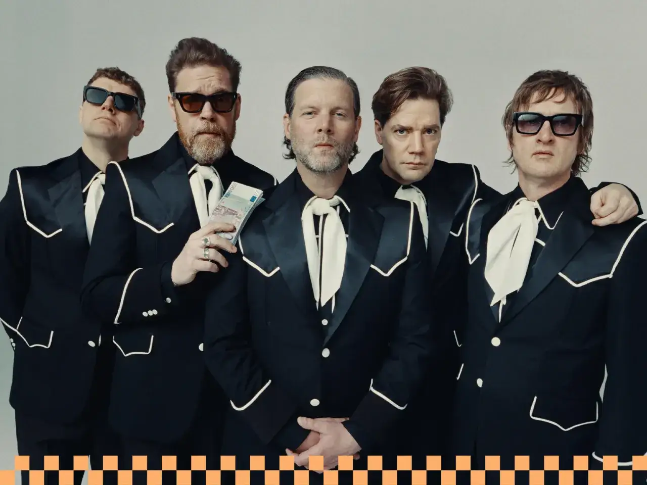 Les membres de The Hives, cinq hommes en costumes noirs avec des accents blancs, posent ensemble. L'un tient une liasse de billets.