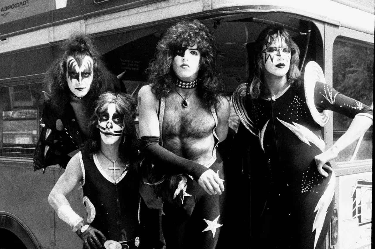Les membres de KISS posent devant un bus, arborant leurs maquillages iconiques et leurs costumes de sc&egrave;ne.
