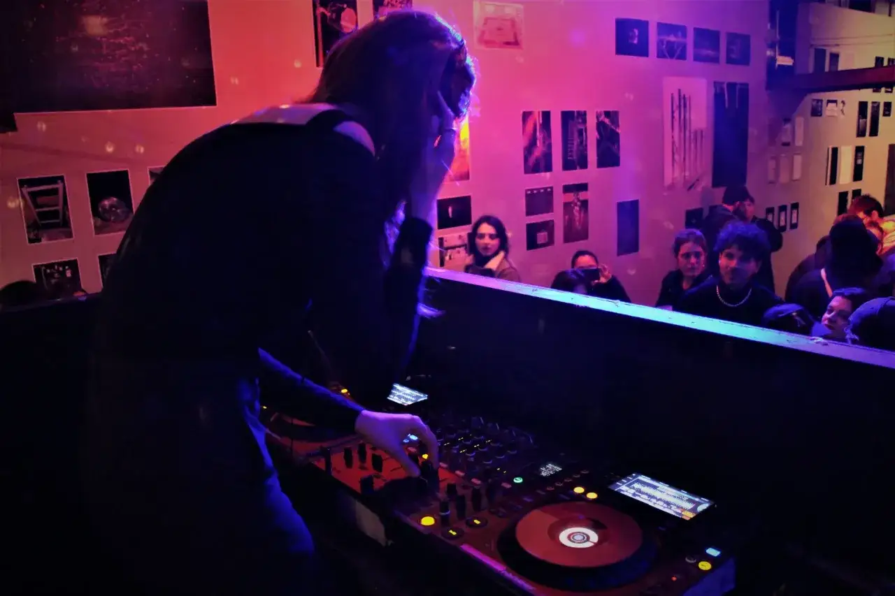 Une DJette aux platines, ambiance clubbing avec de la musique electro. La foule danse au rythme des sons.