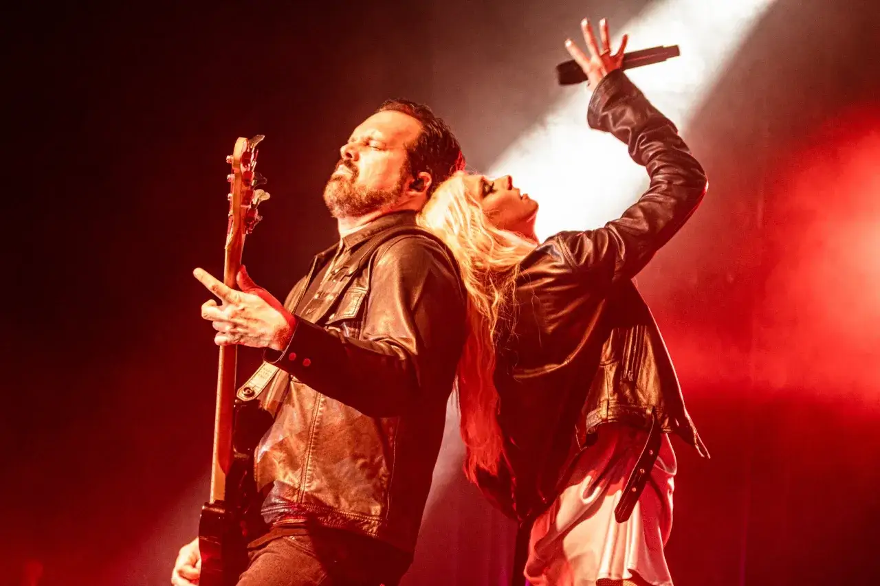 Les membres de The Pretty Reckless, un homme jouant de la guitare et une femme chantant, dos à dos sur scène sous des lumières rouges.