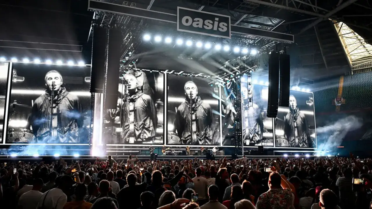 Sc&egrave;ne d'un concert du groupe Oasis, avec Liam Gallagher en gros plan sur les &eacute;crans g&eacute;ants, devant une foule en d&eacute;lire.