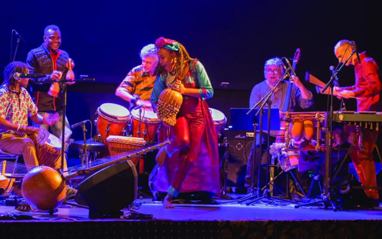 Un groupe africain connu en France, sur scène, joue des percussions et d'autres instruments, créant une ambiance festive.