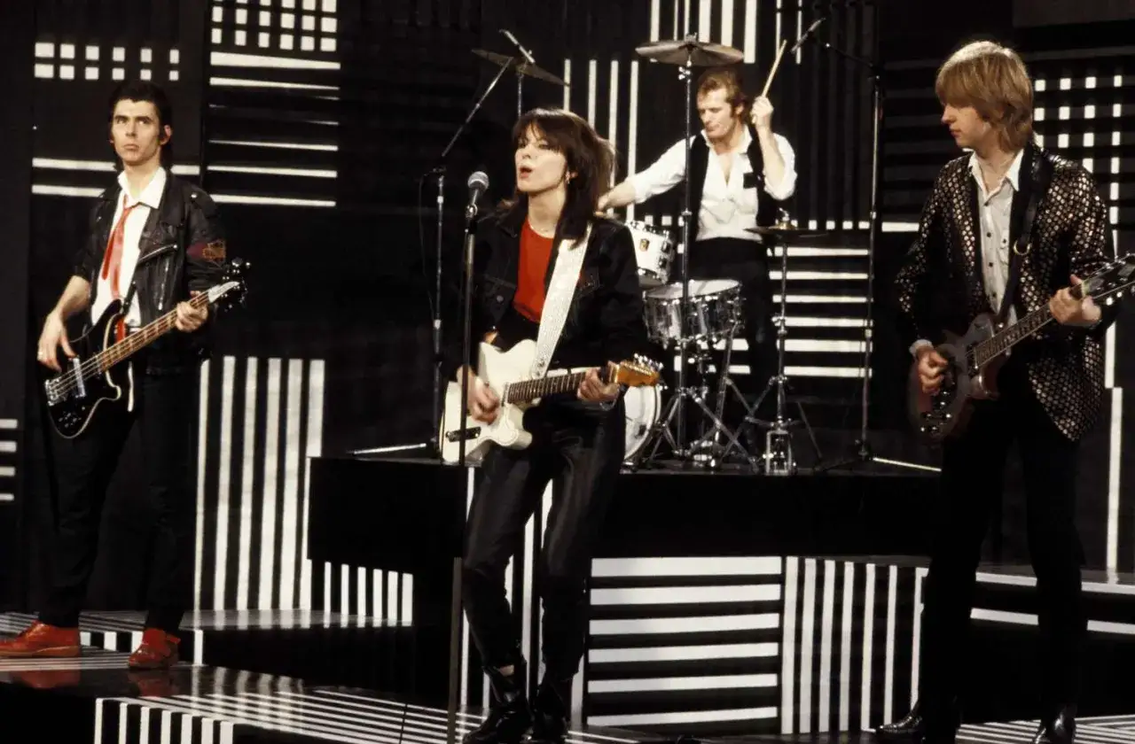 Un groupe hollandais des années 80 sur scène, avec un bassiste, une guitariste chanteuse, un batteur et un guitariste.
