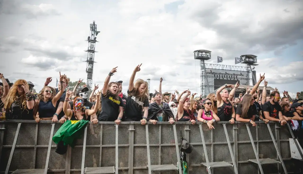 Foule en délire devant une scène, brandissant des signes de rock. Ambiance survoltée pour un groupe metal allemand.