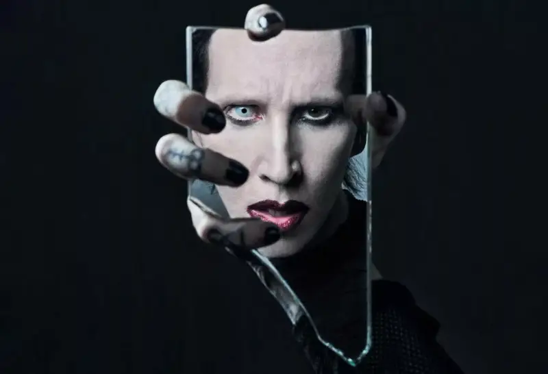Marilyn Manson, visage décomposé dans un miroir brisé, évoquant l'esthétique sombre de ses albums.
