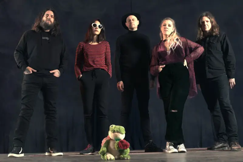 Cinq personnes se tiennent devant un fond sombre. Au premier plan, une grenouille en peluche tient une rose. Le groupe, comme un **crippled black phoenix**, semble prêt à s'envoler.