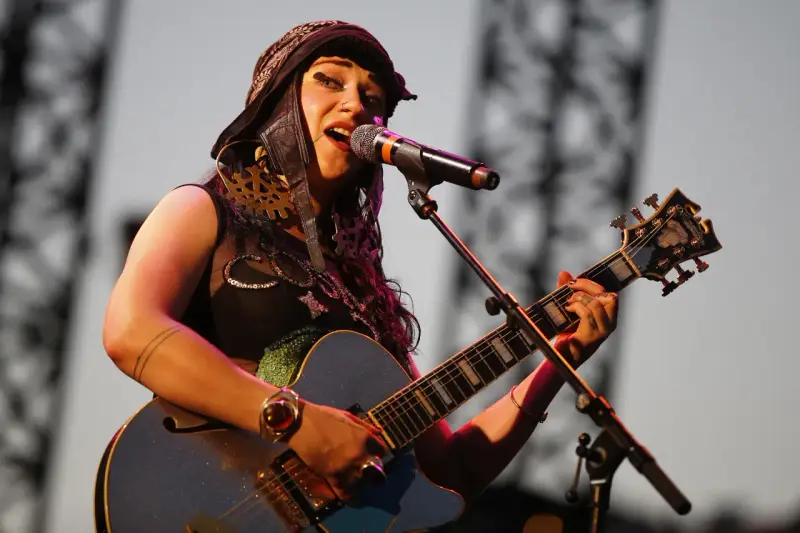 Une artiste de Hiatus Kaiyote, casquette sur la tête, chante et joue de sa guitare bleue étincelante sur scène.
